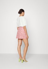 Top curto de mangas curtas brancas combinado com uma saia mini quadriculada em vermelho e branco; sandálias transparentes de salto bloco verde completam o look.