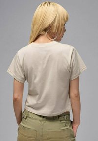 Beige kurz geschnittenes T-Shirt mit kurzen Ärmeln, aus weicher Baumwolle gefertigt. Die Rückseite hat einen runden Ausschnitt und eine glatte Oberfläche, kombiniert mit olivgrünen Hosen.