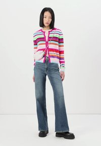 Gestreepte fuzzy cardigan in roze, groen, blauw en paars, gecombineerd met high-waisted flared denim jeans en chunky zwarte platformlaarzen.