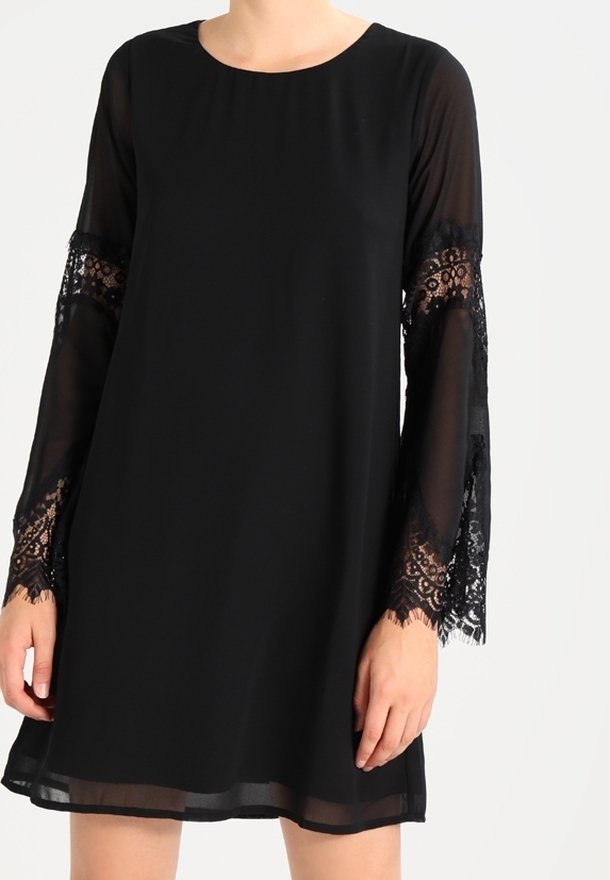 Robe noire à manches longues avec panneaux en dentelle transparente sur les manches et poignets en dentelle, coupe ample, se terminant au-dessus des genoux.