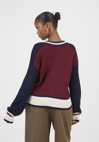 Sweter robiony na drutach w kolorach bordowym, granatowym i kości słoniowej, z prążkowanymi mankietami i luźnym fasonem. Teksturowane panele dodają kontrastu.