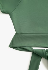 Top verde con lazada frontal hecho de una tela suave y texturizada. Presenta una silueta estructurada con mangas cortas y un detalle anudado en la cintura.