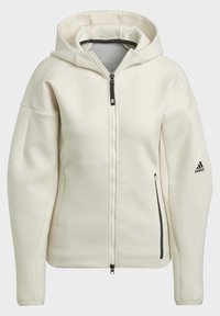 Upnutá bílá bunda s kapucí na zip, dvě přední kapsy, žebrované detaily na rukávech a černé logo Adidas na levém rukávu.