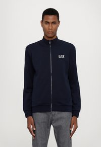 Felpa con zip navy a collo alto, con polsini e orlo a coste, caratterizzata da un logo bianco sul lato sinistro del petto. Tessuto dalla texture liscia.