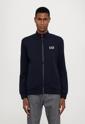 Navy zip-up sweatshirt with high collar, ribbed cuffs and hem, featuring a white logo on the left chest. Smooth fabric texture.