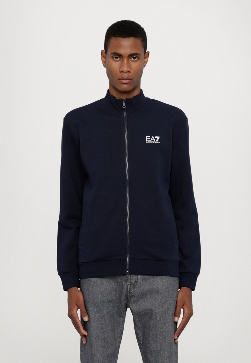 Felpa con zip navy a collo alto, con polsini e orlo a coste, caratterizzata da un logo bianco sul lato sinistro del petto. Tessuto dalla texture liscia.