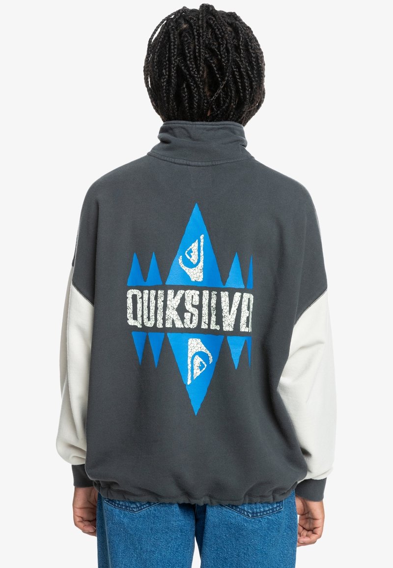 Felpa grigia con colletto alto; presenta motivi a rombi e triangoli blu. Testo e logo "Quiksilver" in bianco, maniche a contrasto.