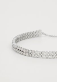 Collier ras du cou en strass avec une base en métal argenté. Présente plusieurs rangées de pierres rondes étincelantes, une texture lisse et un fermoir sécurisé.