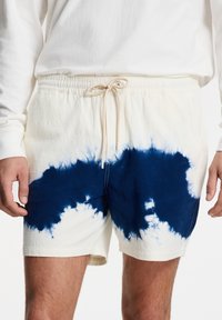 Pantalones cortos tie-dye en crema y azul oscuro, con una cinturilla elástica y cordón, fabricados en un suave tejido texturizado.