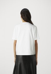T-shirt en coton blanc à manches courtes et col rond, associé à une longue jupe en cuir noir avec des détails de couture.