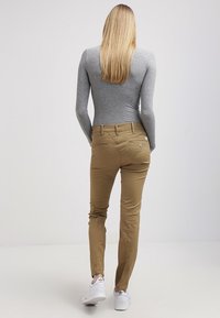 En passande grå långärmad topp i kombination med beige slim-fit byxor. Byxorna har dekorativa sömmar och två bakfickor, stylad med vita sneakers.