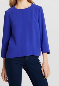 Top leggero blu royal con collo tondo, maniche a tre quarti e una texture liscia, abbinato a jeans in denim scuro.