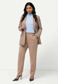 Blazer a scacchi marrone sopra un dolcevita azzurro chiaro, abbinato a pantaloni beige e scarpe con tacco alte blu navy. Tessuto morbido e vestibilità su misura.
