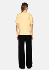 Yellow cotton t-shirt with short sleeves and a relaxed fit, paired with black wide-leg pants featuring white side stripes.