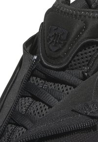 Svart idrottssko med ovandel i mesh, texturerade detaljer, säkrad med dragkedja och bold logodetalj på lateralsidan.