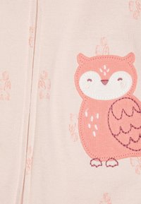 Bleg rosa stof med en broderet ugle-design i blød rosa og hvid. Uglens ansigt er rundt, den har store øjne og detaljerede vinger.