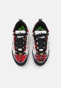 Zapatillas deportivas con un esquema de colores blanco y negro, un patrón a cuadros rojo y amarillo, cordones negros y un acento de logo dorado.