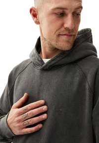 Huppari tummanharmaasta kankaasta, jossa on pehmeä tekstuuri. Ominaisuuksina ribbikujat, kenguru-tasku ja brodeerattu logo rinnassa.