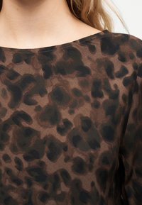 Tissu à imprimé animal marron et noir sur un haut à encolure bateau porté par une personne à la peau claire et aux cheveux blonds visibles au niveau de l'épaule.