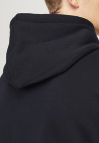 Sort bomulds hoodie med en stor, blød hætte, synlig syning langs kanten og et glat, tekstureret stof.