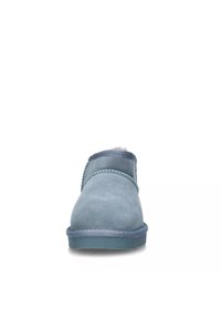 Scarpa slip-on in suede blu con punta arrotondata, superficie testurizzata e una morbida fodera visibile all'apertura. Suola in gomma e dettagli cuciti.