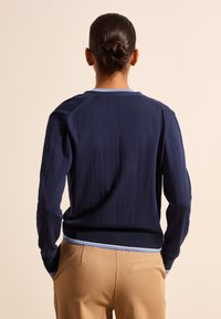 Maglione blu navy a collo rotondo, con bordature azzurro chiaro e polsini a coste. Presenta una vestibilità rilassata e una trama liscia, mostrando la vista posteriore.