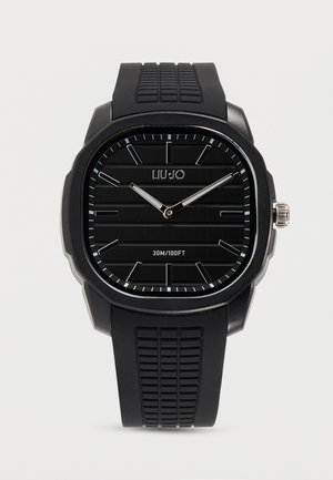 Μαύρο τετράγωνο ρολόι με υφασμένο λουράκι, ασημένιους δείκτες, ελάχιστους δείκτες ώρας και ένδειξη αντοχής στο νερό "30M/100FT" στο καντράν.