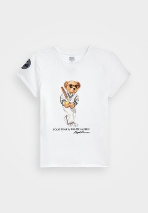 Camiseta blanca de manga corta con un oso que lleva gafas de sol, un atuendo de tenis sosteniendo una raqueta, y el texto "Polo Bear by Ralph Lauren" debajo.
