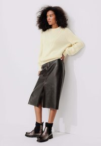 Pull en tricot crème avec un décolleté en V, associé à une jupe midi en cuir noir avec une fente à l'avant. Bottines noires avec accents côtelés.