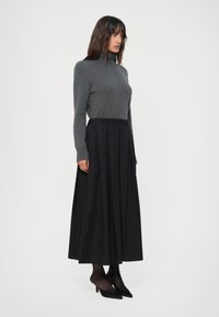 Grå turtleneck-genser kombinert med et svart plissé skjørt. Outfiten har lange ermer, en tettsittende overdel og en svingende skjørtedesign.