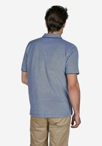 Blaues Poloshirt mit kurzen Ärmeln, strukturiertem Stoff und kontrastierendem Kragen. Kombiniert mit hellbeigen Hosen. Sichtbare Nahtdetails am Saum.