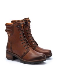 Bottes en cuir marron montant jusqu'à la cheville, avec un laçage, un talon carré, un col rembourré et des coutures décoratives sur les côtés.
