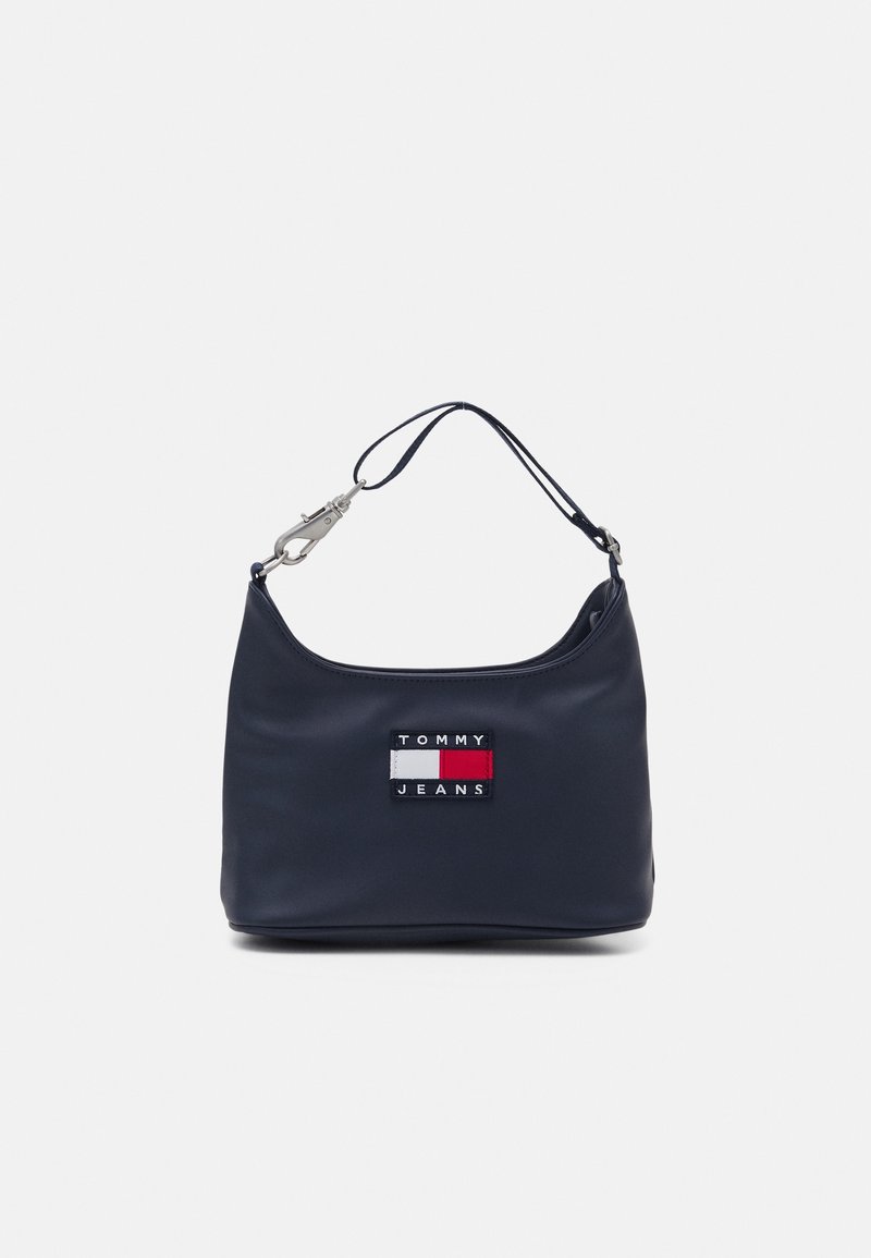 Sac à main bleu marine avec une courte bandoulière et une fermeture métallique, orné d'un patch logo Tommy Jeans avec des blocs de couleur rouge, blanc et marine.