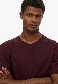 Bordeauxrode katoenen t-shirt met een ronde hals, korte mouwen en een klein logo op de borst. Glad oppervlak, ontspannen pasvorm.