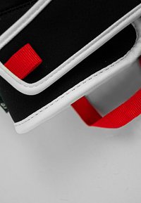 Materiale in tessuto nero con cuciture bianche, caratterizzato da un'etichetta rossa prominente e un'inserto testurizzato vicino al bordo.