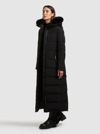 Čierna pufovaná bunda s dlhým, priliehavým strihom, s kapucňou podšitou umelou kožušinou a prešívanou štruktúrou. Zips a bočné vrecká, v páre s čiernymi čižmami.