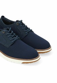 Zapatos de malla azul marino con un empeine texturizado, punteras redondas y suelas de goma blanca en contraste. Incluyen cierre con cordones y costuras decorativas.