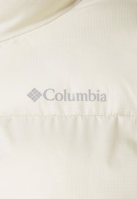 Tejido acolchado de color crema con un sutil patrón de cuadrícula; presenta el logotipo de Columbia en gris, ubicado cerca del centro superior.
