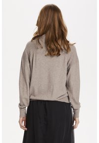 Beige polokrage tröja med ribbad textur och sänkt axelparti, kombinerad med en svart kjol, sedd från baksidan.