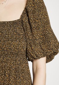 Svart tygklänning med smockade byst och puffärmar, med ett mönster av bruna och krämiga prickar över hela ytan. Texturerad utseende.