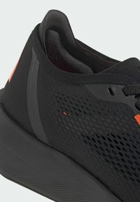 Black athletic shoe with mesh upper and smooth synthetic accents. Features a textured rubber sole and a small orange detail on the side.