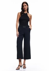 Svart ribbad halterneck-top som kombineras med högmidjade svarta vida byxor med en spännbälte. Modellen bär strappy svarta högklackade sandaler.