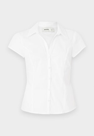 Biela blúzka s krátkym rukávom a golierom, priliehavého strihu s dvoma radmi gombíkov na prednej strane. Hladká bavlnená textura.