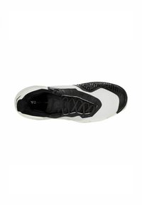 Zapatilla deportiva en blanco y negro con parte superior de malla, acentos texturizados, puntera de goma negra y suela con patrón. Presenta un diseño con cordones.