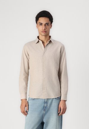 Chemise beige clair à manches longues avec un col boutonné, fabriquée dans un tissu texturé, présentant une coupe droite et des boutons sur le devant.