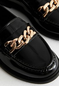 Mocassini neri in vernice con un accento in catena dorata sulla tomaia, dal design liscio e con punta arrotondata.