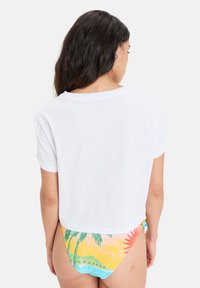 White cropped t-shirt with short sleeves; paired with multicolored bikini bottom featuring palm tree and sun graphic designs.