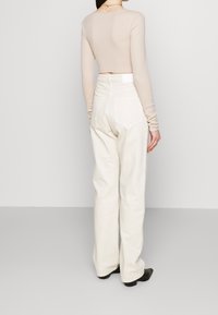 Haut à manches longues beige clair et jeans blancs à jambes larges, comportant des poches arrière et une finition texturée. Haut ajusté au design court.