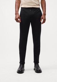 Black sweatpants with a drawstring waist, featuring a tapered leg design and a smooth texture. Worn with black ankle boots.