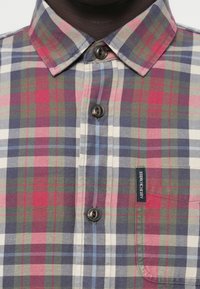 Chemise à carreaux avec des tons de bleu, vert et rouge. Fabriquée dans un tissu à texture douce, elle comprend une poche poitrine et une étiquette de logo.